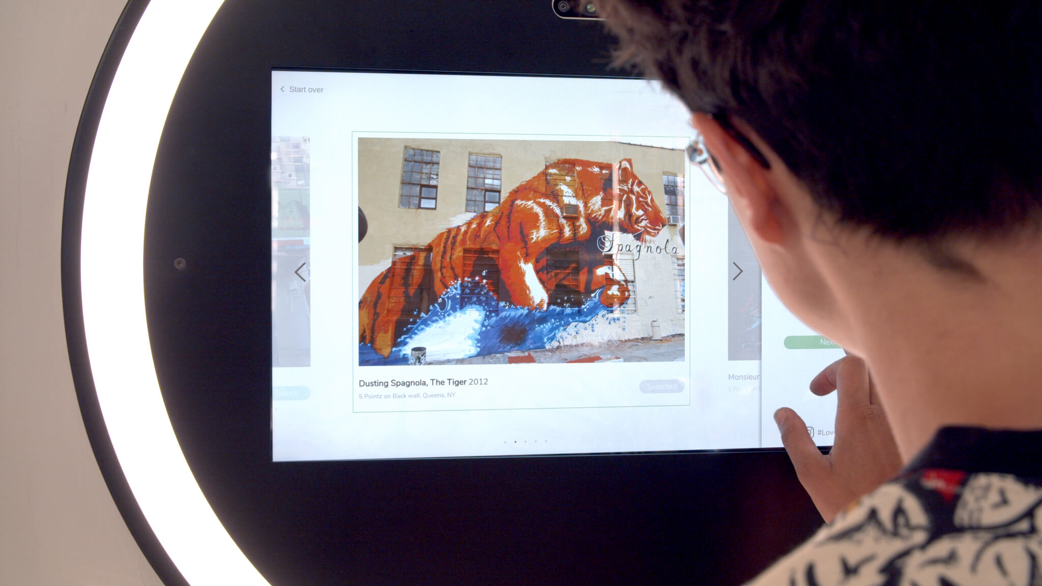 A woman presses a touch display with a tiger on it on a machine learning media wall mural.